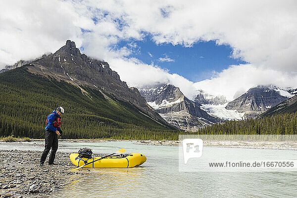 Man exploring the Rocky Mountains in a packraft stops for a break.