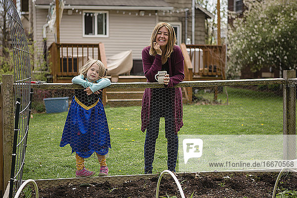 Eine Mutter und ein kleines Mädchen im Prinzessinnenkleid stehen am Rande eines Gartens