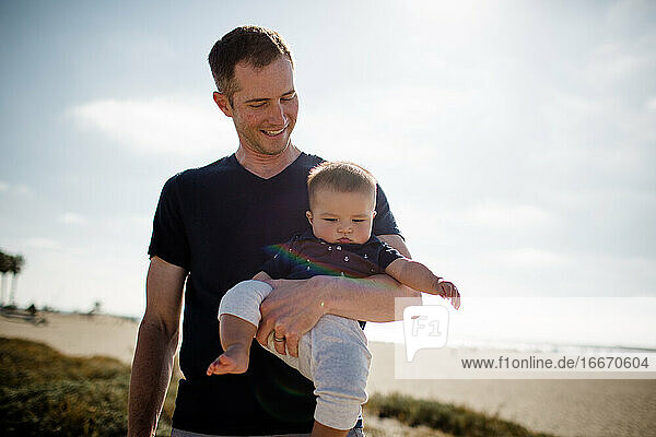 Vater lächelt und hält seinen Sohn lässig am Strand