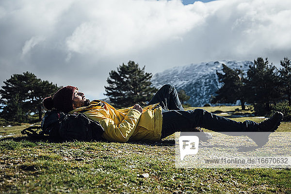 Junger Mann mit gelber Jacke und Rucksack auf dem Berg liegend.