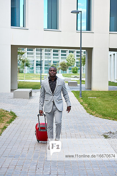 African-American in a white suit and a red suitcase.