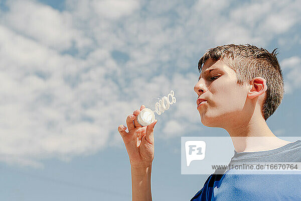 Junger weißer Junge bläst eine Seifenblase im Freien mit Himmel im Hintergrund