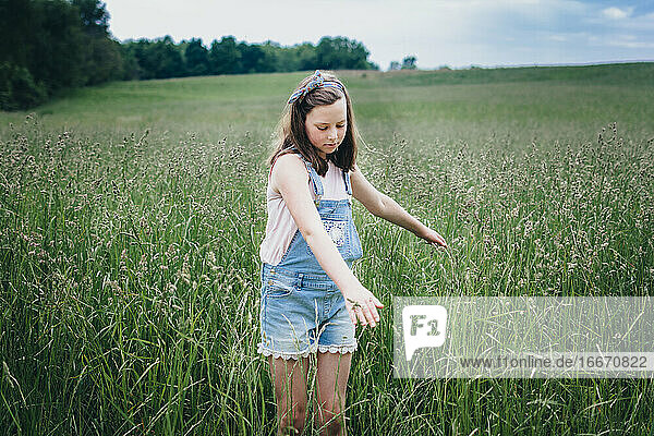 Mädchen läuft mit den Händen durch hohes Gras auf einem Feld im Mittleren Westen