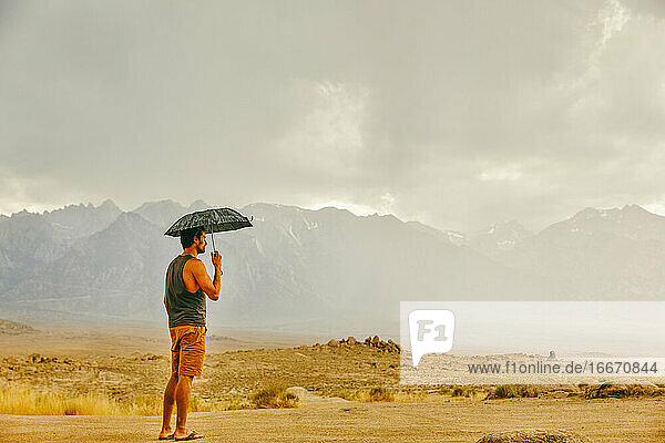 Young man in desert of northern California  holding umbrella in rain.
