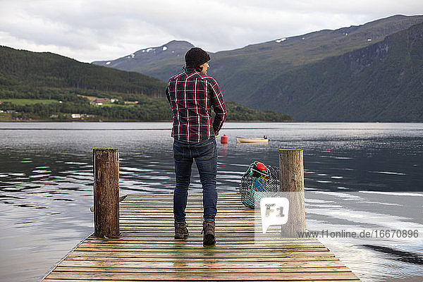 Ein Fischer zieht seine Handschuhe auf einem Steg in einem Fjord an