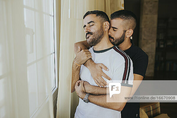 homosexual couple hugging at home by the window
