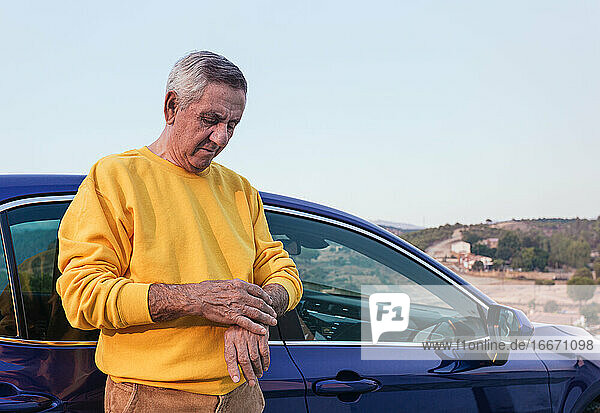 Älterer Reisender  der in der Nähe des Autos die Zeit kontrolliert