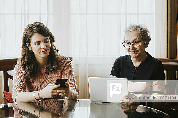 Enkelin mit Handy und Großmutter mit Tablet