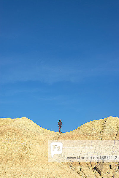 Vorderansicht einer Frau auf einem Hügel  die mit den Händen in den Taschen steht und zum Horizont schaut