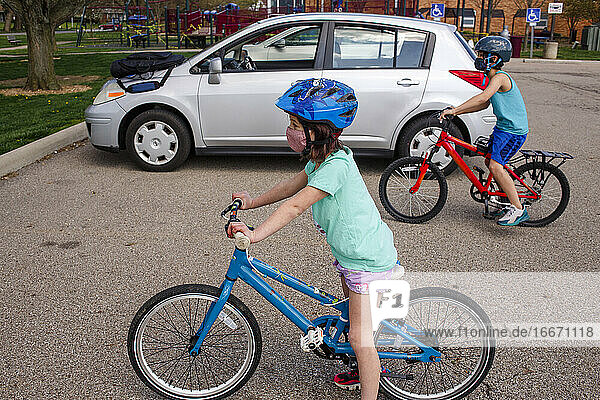 Ein Junge und ein Mädchen mit Gesichtsmasken fahren zusammen auf einem Parkplatz Fahrrad