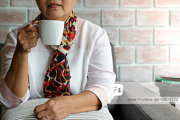 Alte Frau hält eine Tasse heißen Kaffee zu Hause trinken