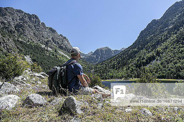 Male backpacker tourist in Spain looking at landscape while sitting on the rock in front of a lake.Mountain Pyrenees.