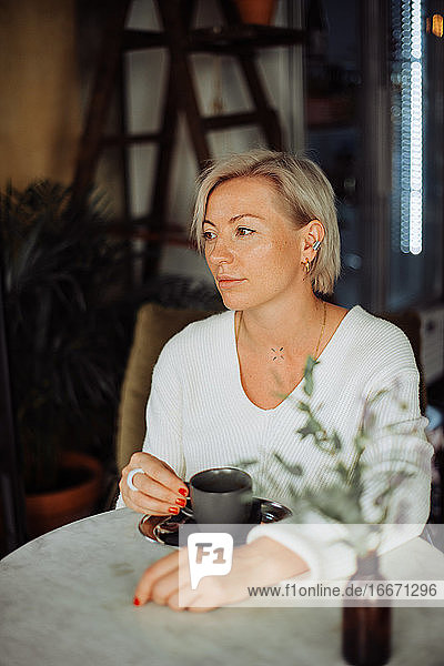 Blonde stilvolle Frau sitzt allein am Tisch mit einer Tasse Kaffee
