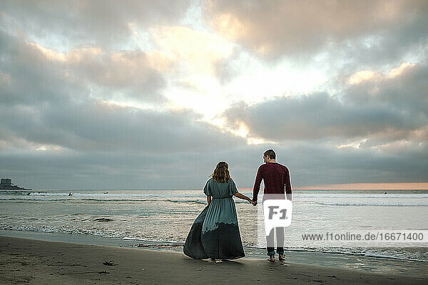 Romantisches Paar hält Hände am Strand bei Sonnenuntergang