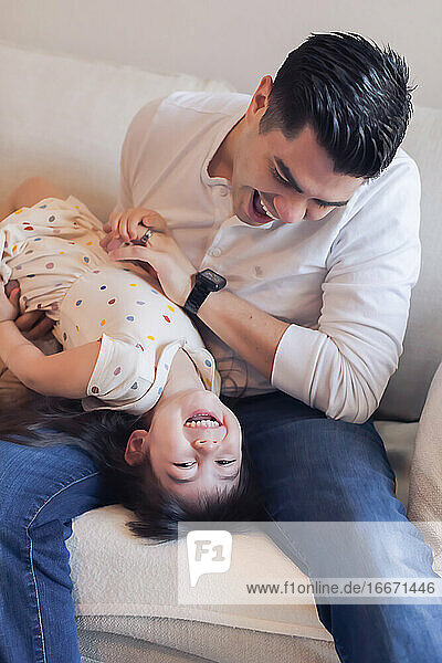 Papa kitzelt kopfüber 4 Jahre alte Tochter auf der Couch