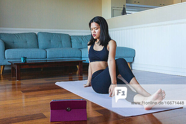 Frau benutzt digitales Tablet  um zu Hause Yoga zu praktizieren
