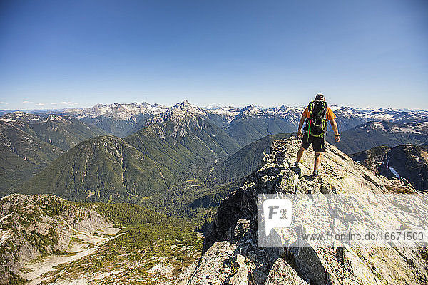 Rückansicht eines Rucksacktouristen beim Wandern auf dem Gipfelgrat mit Aussicht.
