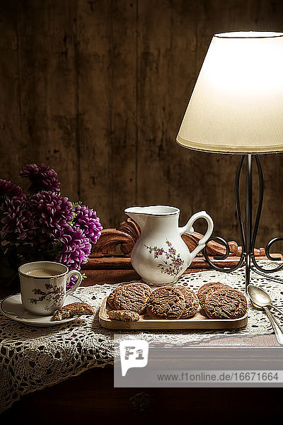 Selbstgebackene Kekse mit Kaffee auf einem rustikalen  mit einer Lampe beleuchteten Tisch