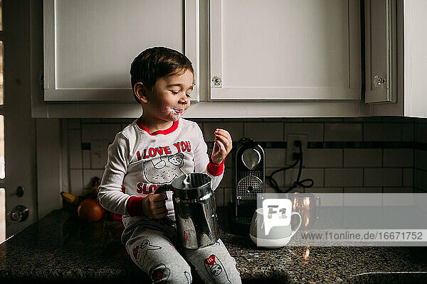 Junge im Vorschulalter sitzt auf dem Küchentisch mit Milch im Gesicht