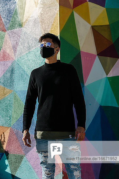 boy with sunglasses and mask posing in front of a painted wall