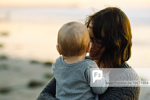A mother holding her son lovingly during a sunset on the beach in cali