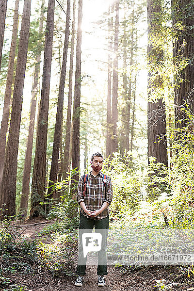 Teenage person standing in redwood grove with mask during COVID-19