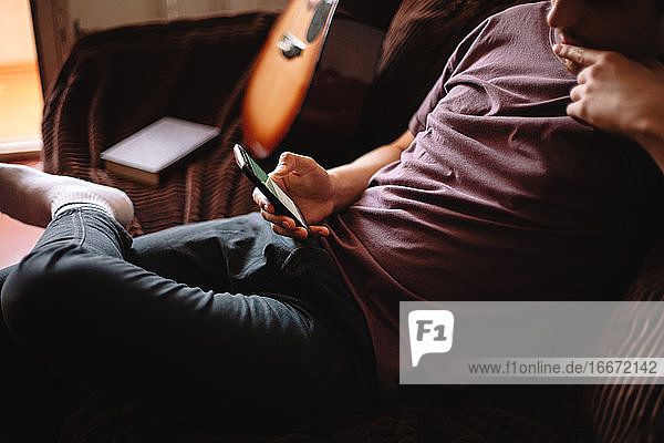 Nachdenklicher junger Mann benutzt sein Smartphone  während er zu Hause sitzt