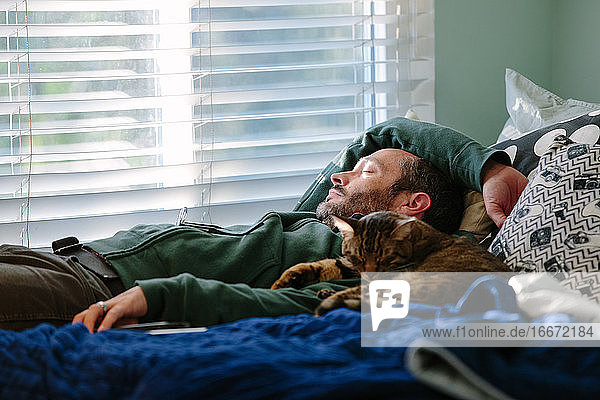 Mann macht ein Katzennickerchen mit seiner getigerten Katze  die neben ihm kuschelt