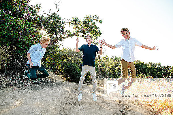 Three Boys Jump In The Air Smiling While On A Hiking Trail
