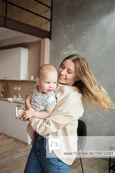 Lächelnde Frau hält in den Händen Baby-Mädchen im Wohnzimmer. Kindermädchen  Kind.
