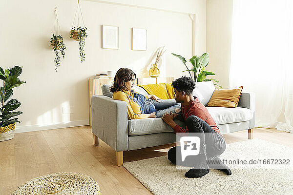 Ehemann streichelt den Bauch seiner schwangeren Frau auf einem Sofa. Interracial Paar Konzept