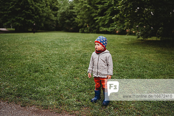 Young boy with serious face standing at the park looking to the side