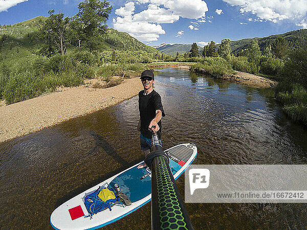 Smiling man taking selfie while paddleboarding on river