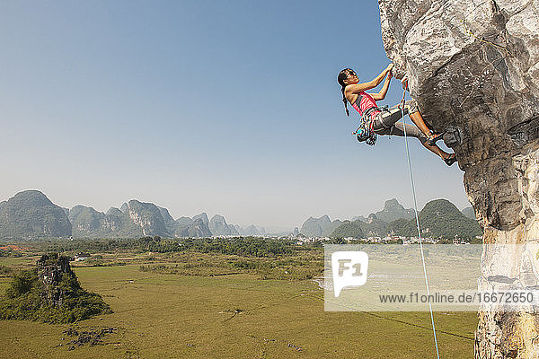 Bergsteigerin zieht sich an einem überhängenden Felsen in Yangshuo / China hoch