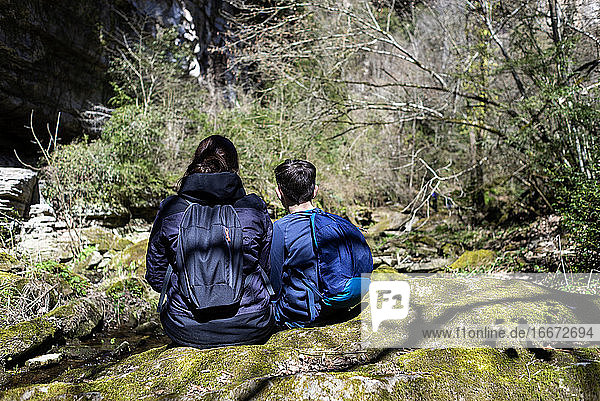 Back view of two young teenagers sitting on river shore