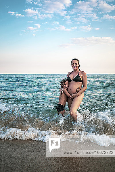 5 Jahre altes Kind  das seine schwangere Mutter umarmt  knietief im Meer
