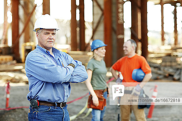Porträt eines männlichen Bauführers mit zwei Arbeitern dahinter