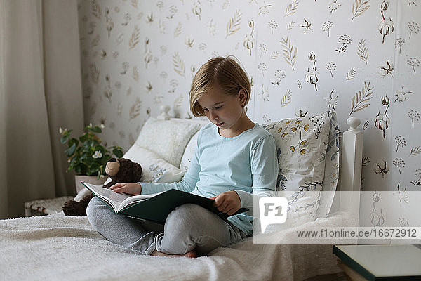 Ein russisches Mädchen liest auf ihrem Bett in einem hellen Zimmer ein Buch.