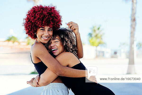 Two attractive latin girls with afro hair hugging each other amicably.