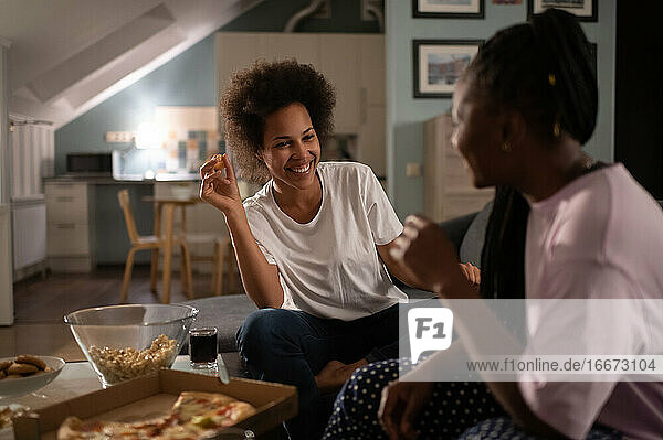 Laughing girlfriends having delivered pizza and chatting on home party