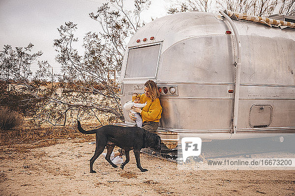 A woman with a baby and a dog is near an RV trailer  California