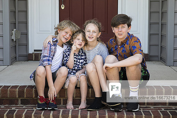 Vier Geschwister sitzen zusammen auf einer Backsteintreppe in nicht zusammenpassenden Outfits