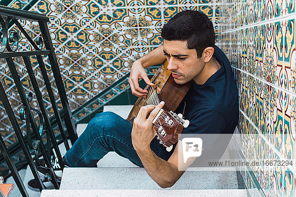 Fokus Mann spielt Gitarre und sitzt auf einer Treppe mit schönen Fliesen.
