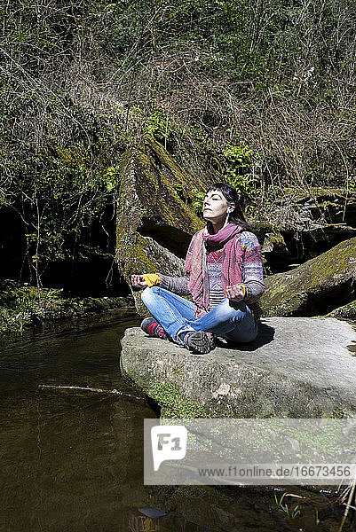 Junge Frau beim Meditieren auf einem Stein am Flussufer.