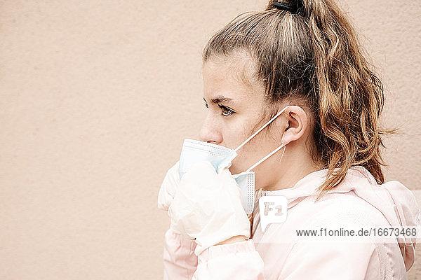 Ein blondes Mädchen mit Latexhandschuhen und Gesichtsmaske zeigt  wie sie sich vor Coronaviren  Bakterien  Viren  Pilzen usw. schützt. Sie nimmt die Maske ab  um einen klaren Atem zu bekommen. Horizontal