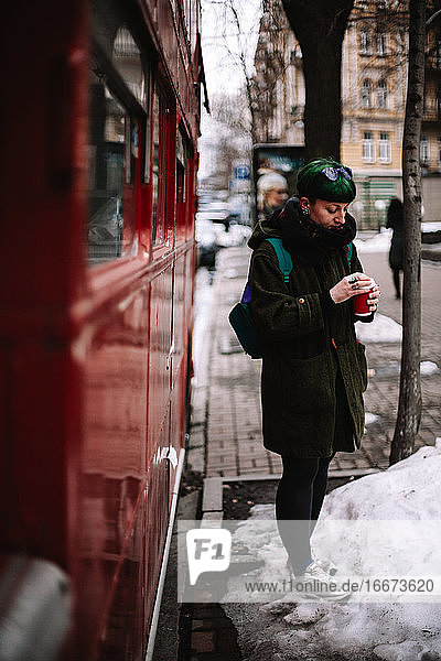 Porträt einer nicht-binären Hipster-Frau  die an einem roten Bus in der Stadt steht