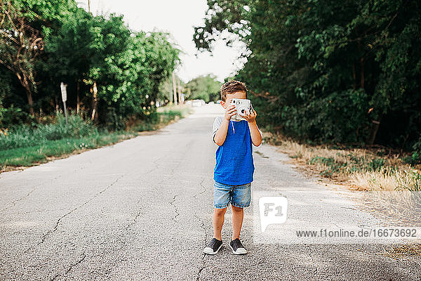 Young boy standing outside taking photo with instant camera