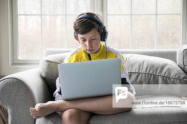 Junge mit Laptop für virtuelle Schule sitzt auf der Couch im Wohnzimmer