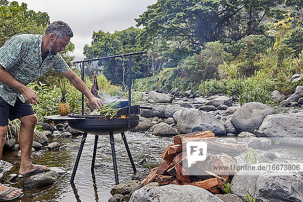 Chefkoch kocht über offener Flamme in der Campingküche am Bach