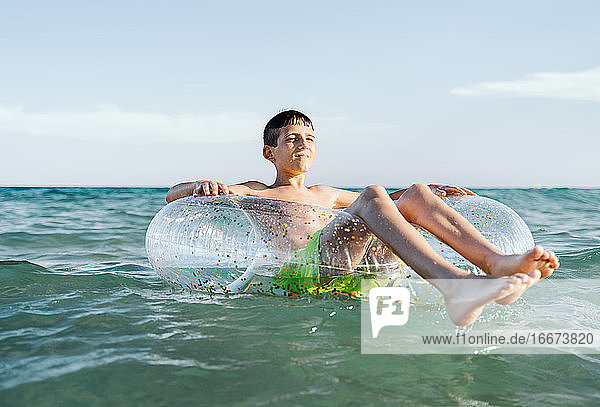 entspannter weißer Junge schwimmt in einem Schwimmer im Meer und genießt die ruhigen Wellen im Sommer